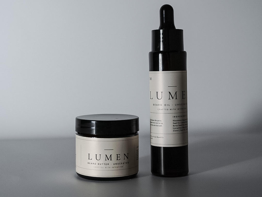 LUMEN unscented beard oil and beard butter set in amber glass packaging on a soft gray background with natural directional light.