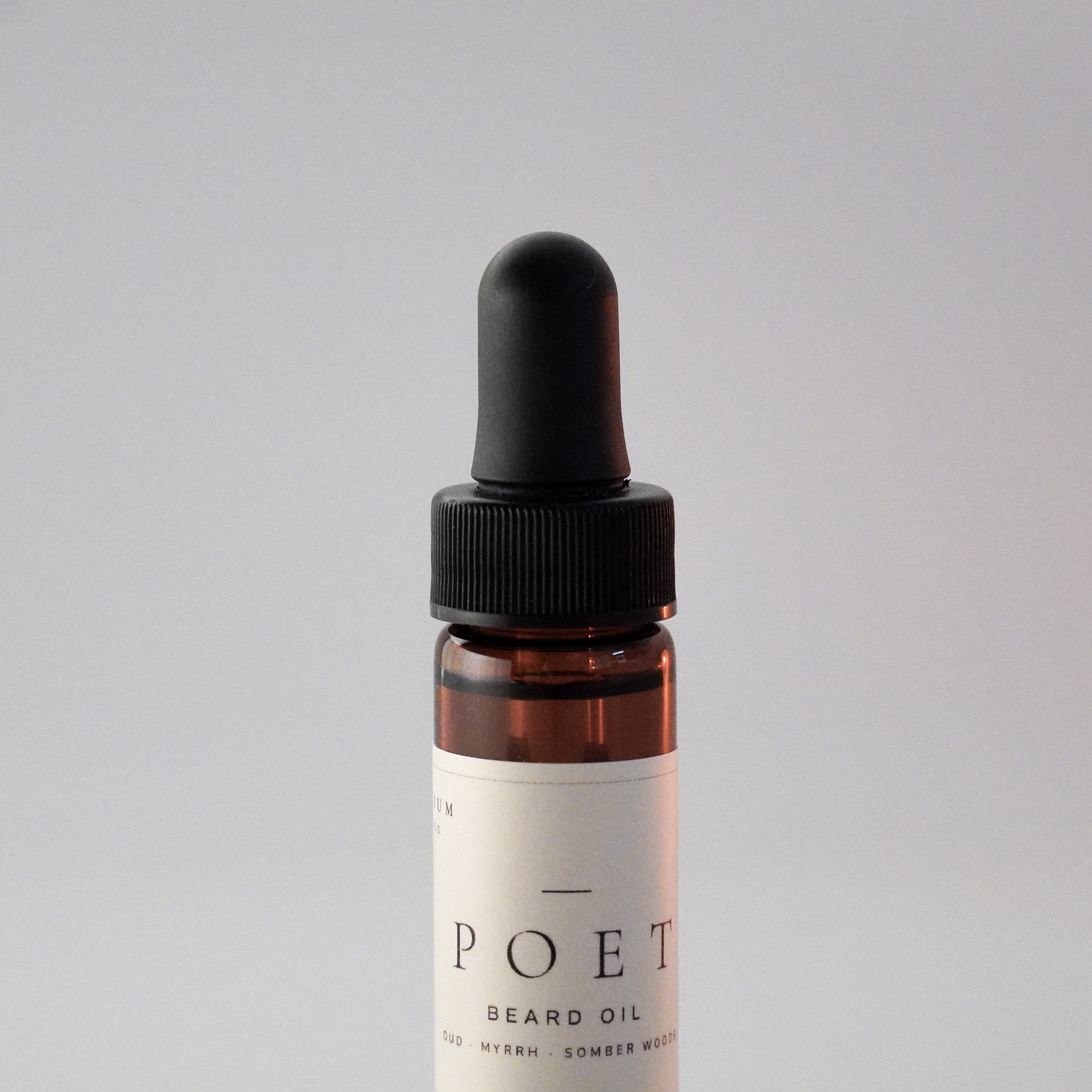 Close-up of The Poet 15 ml beard oil bottle showing the dropper, amber glass, and label.