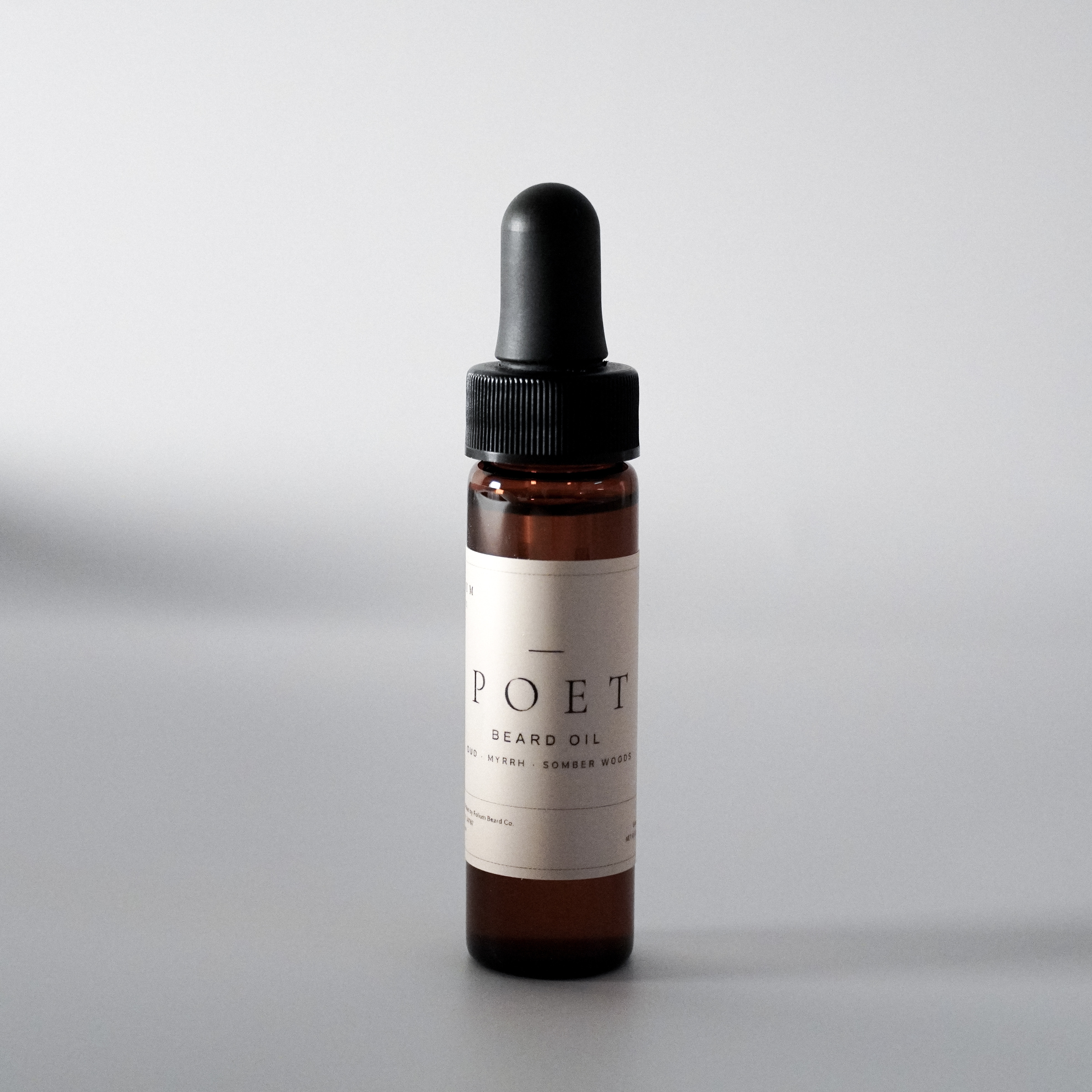 The Poet oud and myrrh beard oil in a 15 ml bottle on a cool grey background.