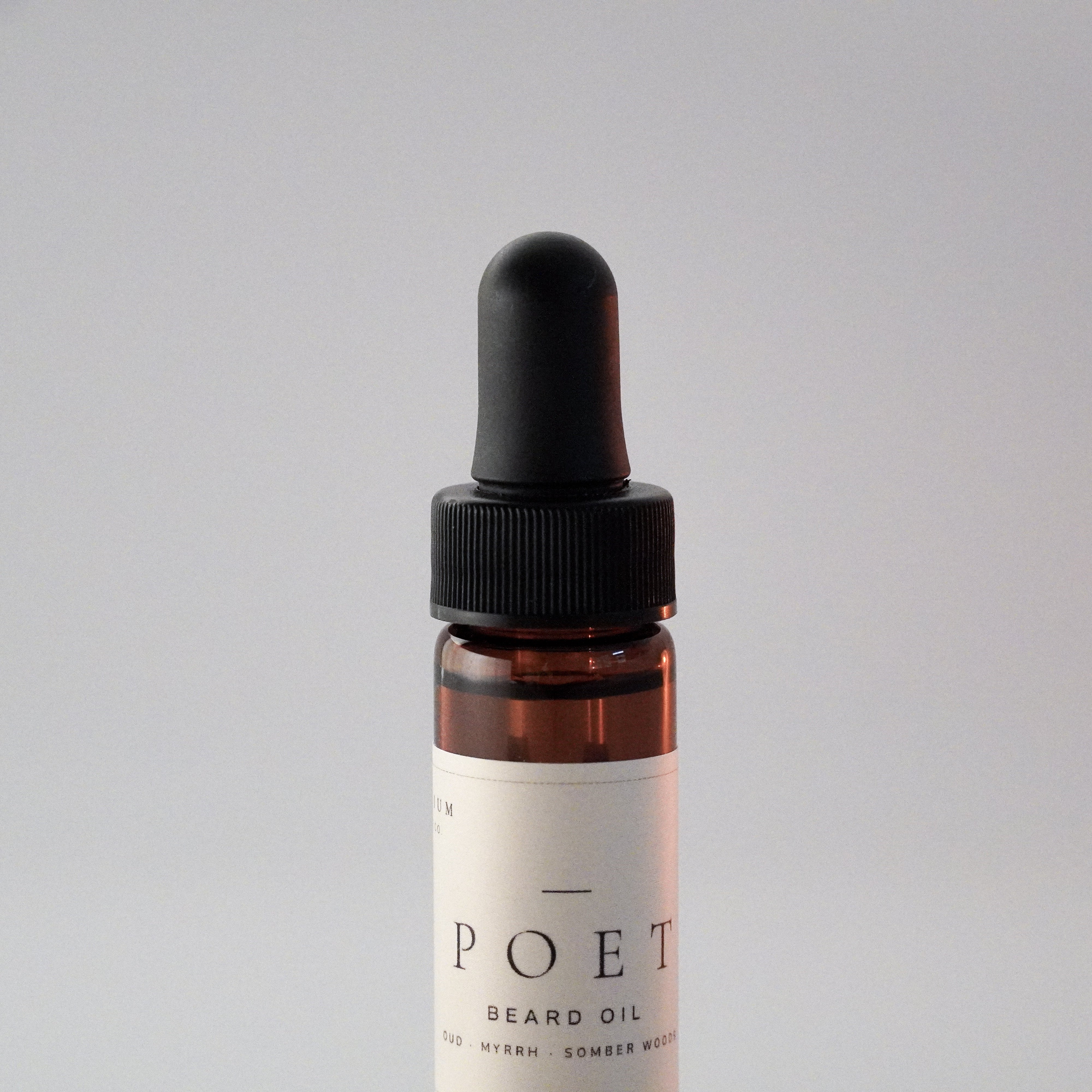 Close-up of The Poet 15 ml beard oil bottle showing the dropper, amber glass, and label.